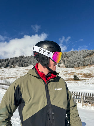 Person wearing a green and black jacket with a Terrex logo, black helmet, and colorful goggles in a snowy landscape.