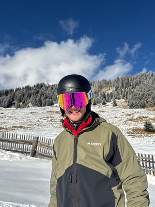 Person in ski gear with colorful goggles standing in a snowy landscape.