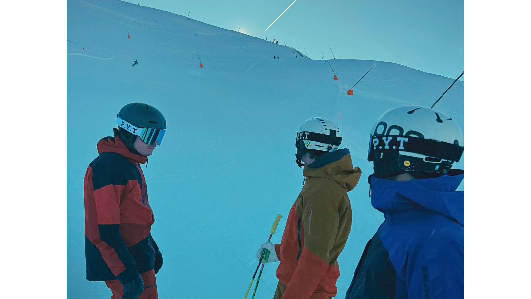 Three skiers on a snowy slope with a clear blue sky.